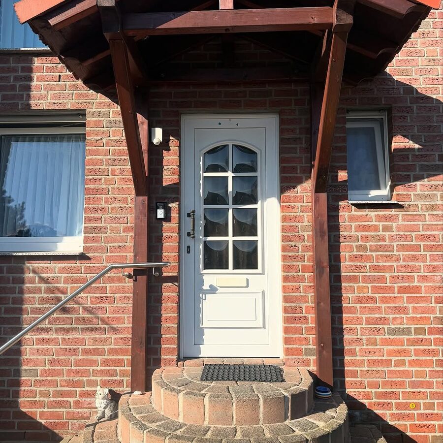 Weiße Haustür unter einem Vordach mit gemauerter Rundtreppe